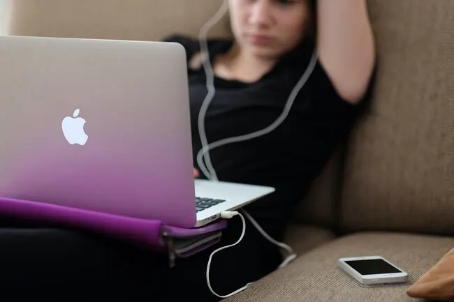 Eine Studentin, die mit Laptop und Kopfhörern auf dem Sofa sitzt