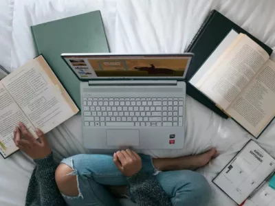 Studierende arbeitet mit Büchern und Laptop auf dem Bett