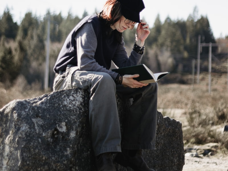 Eine Person sitzt auf einem Felsen und liest ein Buch