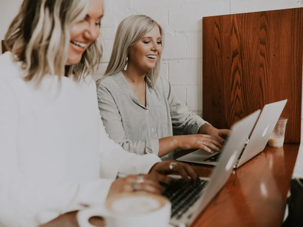 Ein paar Frauen sitzen mit Laptops an einem Tisch.