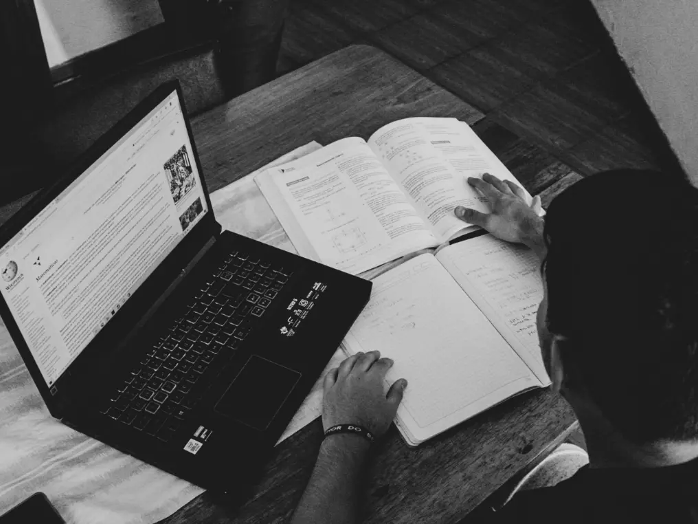 Student mit Laptop und Buch lernt am Tisch