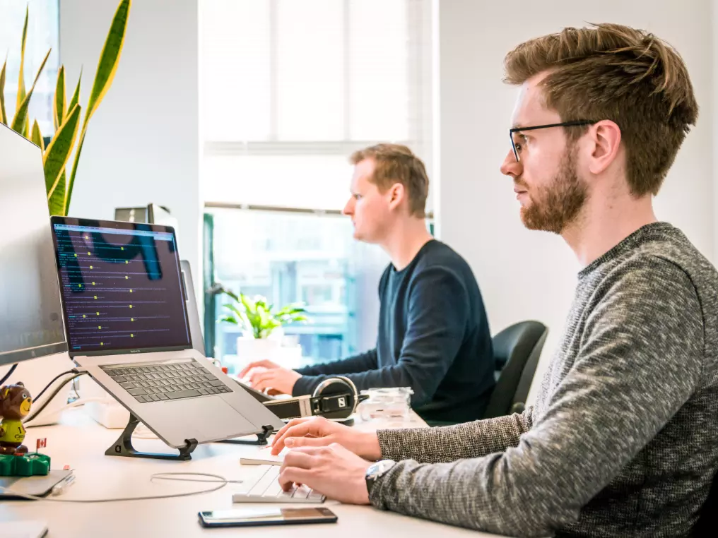 Zwei Männer sitzen an einem Schreibtisch und arbeiten an einem Computer.