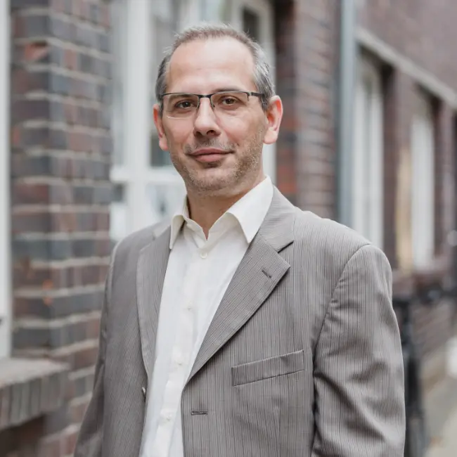 Dr. Frantisek Jelenciak, Professor, steht in Anzug und Brille vor einem Backsteingebäude.