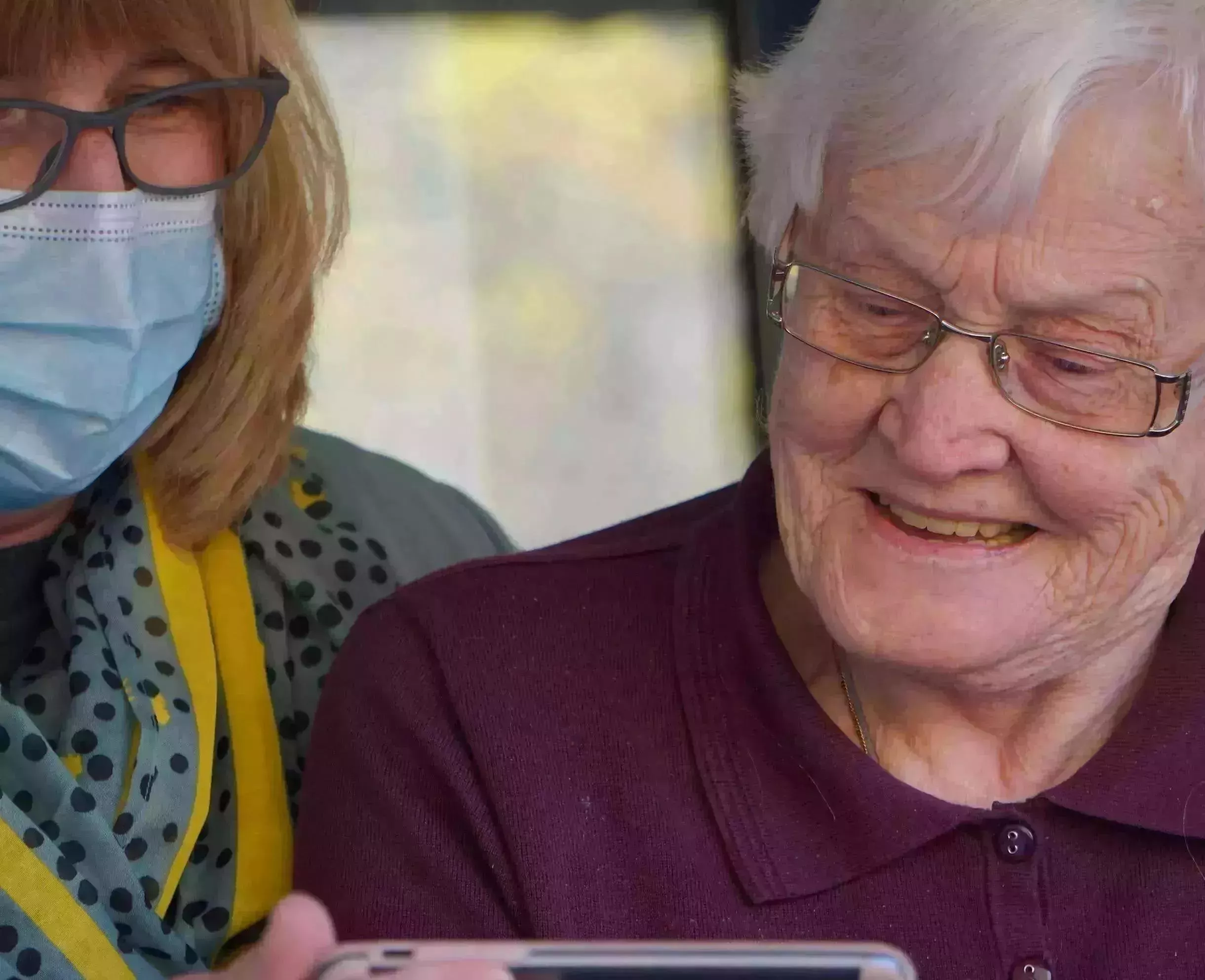 Eine ältere Frau mit Gesichtsmaske blickt auf ein Mobiltelefon.