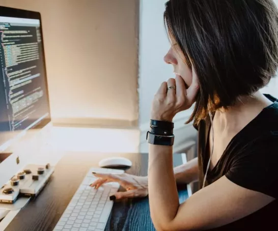 Eine Frau sitzt an einem Schreibtisch vor einem Computer und arbeitet in der Zukunft des Bereichs Wirtschaftsinformatik.