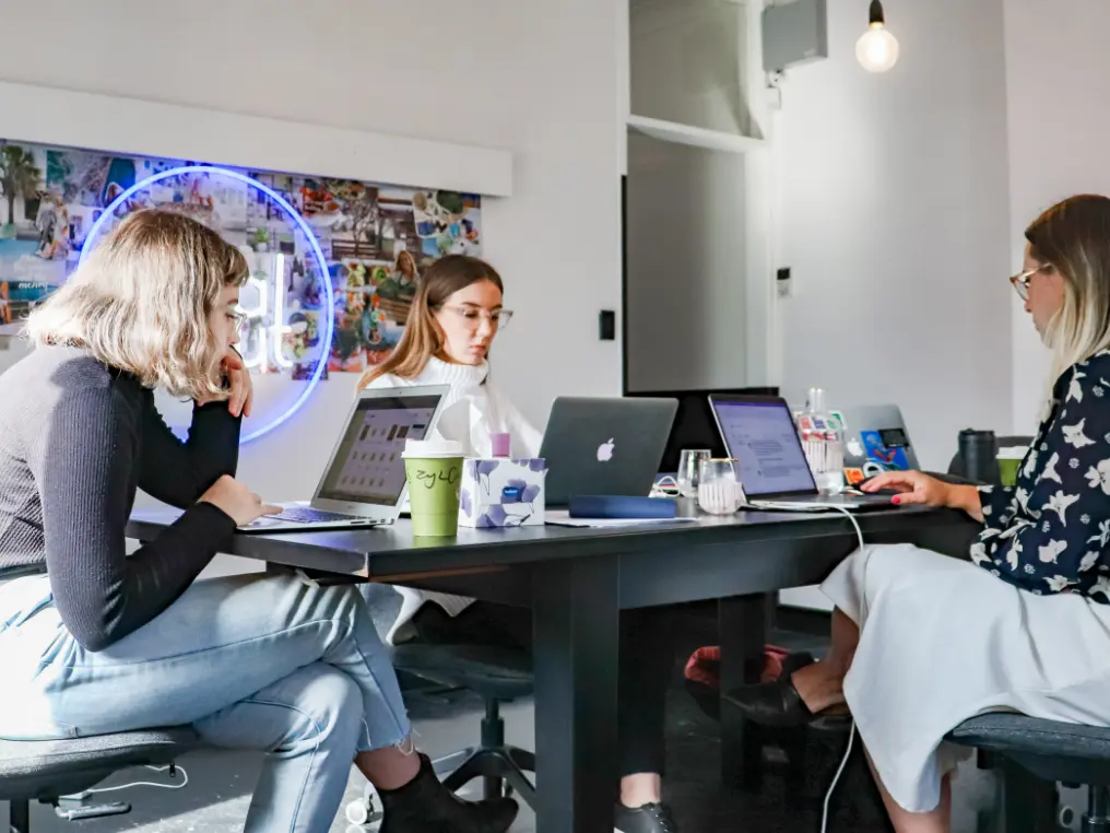 Drei Frauen sitzen mit Laptops an einem Tisch.