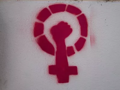 Rote Schablone eines Venussymbols mit Faust auf einer weißen Wand