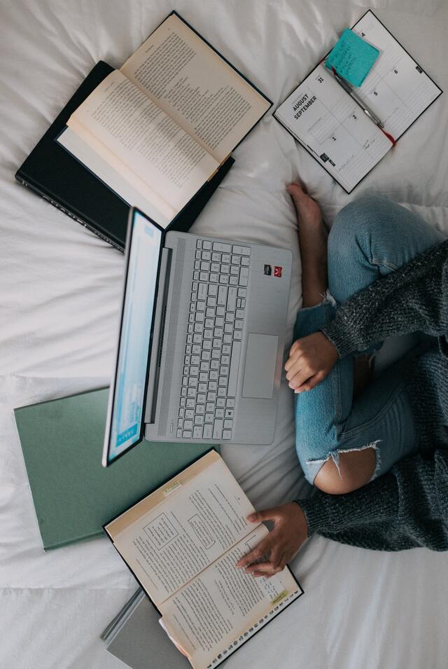 Studentin lernt auf ihrem Bett mit Laptop und Notizen