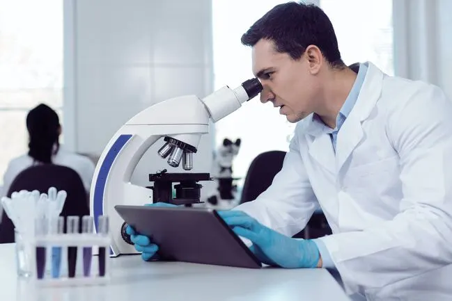 Ein Medizintechniker schaut in ein weißes Mikroskop