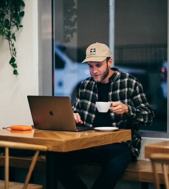 Ein Mann sitzt mit einem Laptop und einer Tasse Kaffee an einem Tisch.