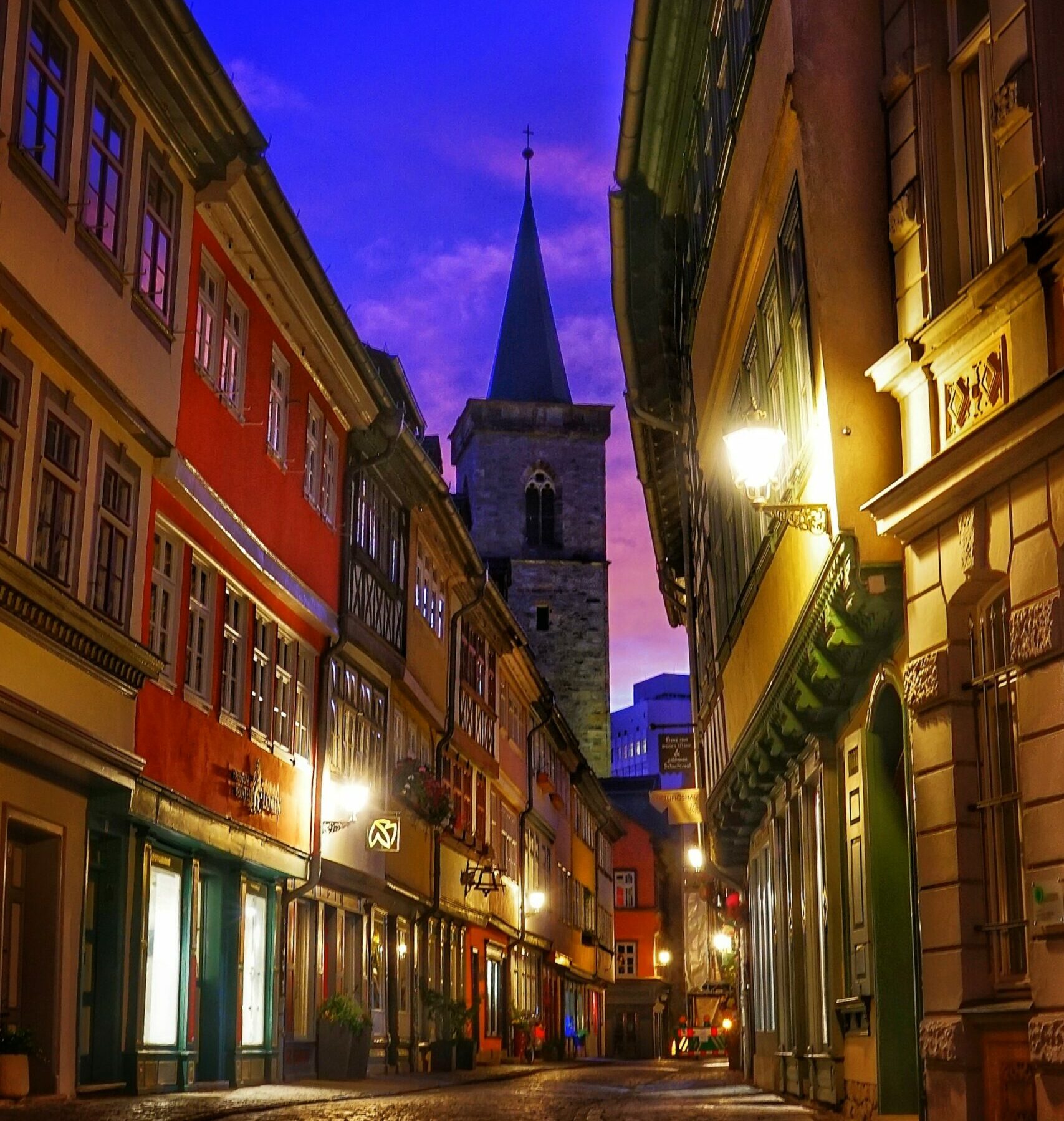 Eine Stadtstraße bei Nacht mit einem Glockenturm im Hintergrund.