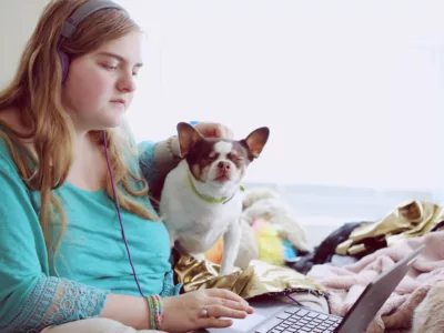 Studentin lernt mit Kopfhörern und Hund in ihrem Bett am Laptop