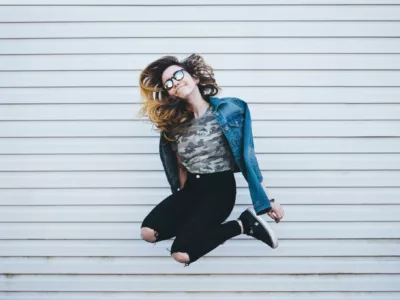 Eine Frau springt vor einer grauen Wand mit angewinkelten Beinen in die Höhe.