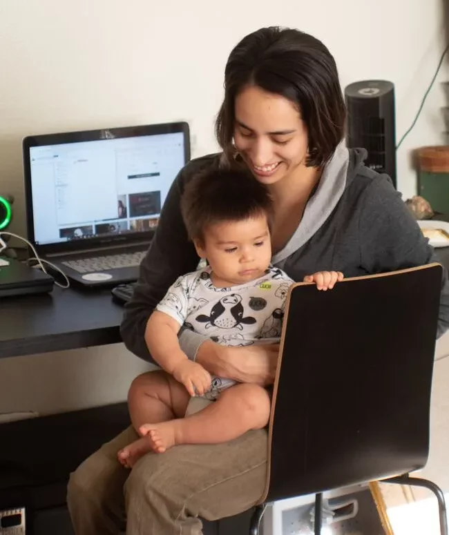 Mutter sitzt mit ihrem Kleinkind vor ihrem Laptop und macht ein Fernstudium