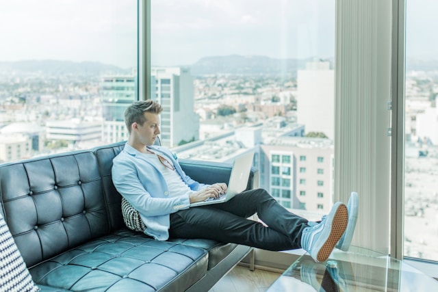 Student sitzt auf dem Sofa mit Laptop auf dem Schoß und Beinen auf dem Tisch