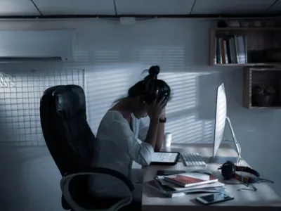 Frau mit Hände am Kopf sitzt im Dunkeln vor ihrem Laptop