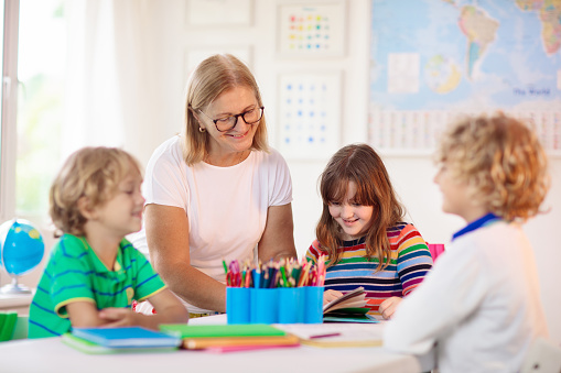 Erzieherin spielt mit Kindern am Tisch mit Stiften.