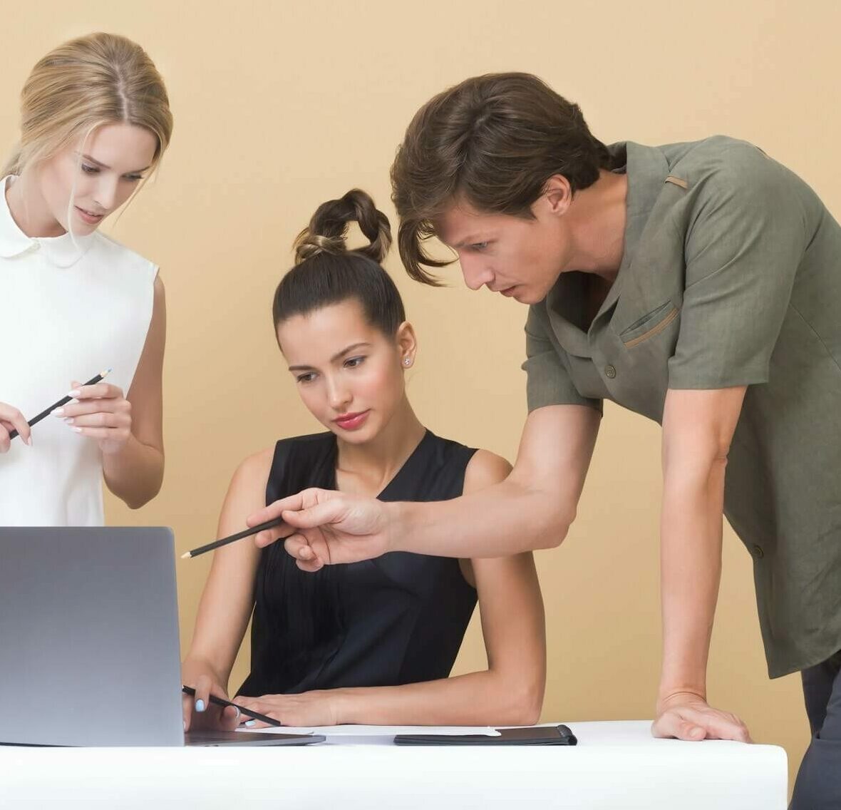 3 Studierende schauen auf einen Laptop, ein Student zeigt mit einem Stift darauf