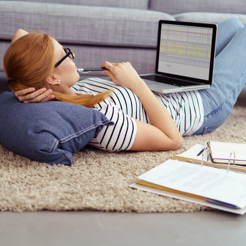 Studentin liegt auf einem Teppichboden und rechnet auf ihrem Laptop