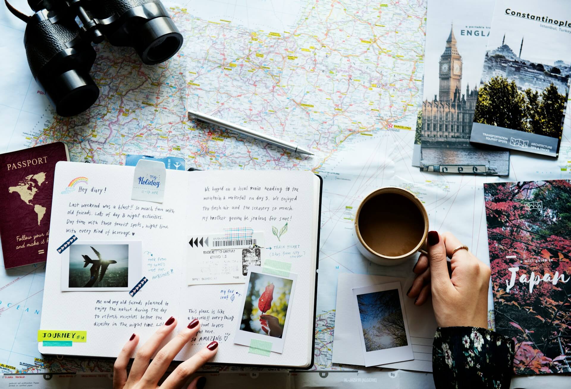 Reiseutensilien auf einem Tisch, darunter Reisepass, Notizbuch, Landkarte, Fernglas und Kaffeetasse.