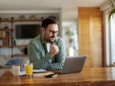 Ein Mann mit Brille sitzt in einem Büroraum am Schreibtisch und arbeitet an seinem Laptop.