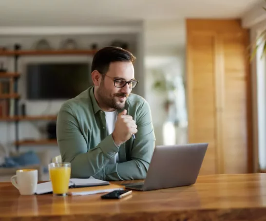 Ein Mann mit Brille sitzt in einem Büroraum am Schreibtisch und arbeitet an seinem Laptop.
