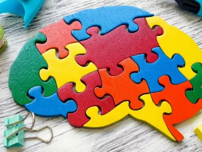 Ein buntes Holzpuzzle liegt auf einem hölzernen Untergrund und sieht aus wie ein menschliches Gehirn. Die Puzzleteile sind in verschiedenen Farben wie Rot, Gelb, Blau und Grün gestaltet.