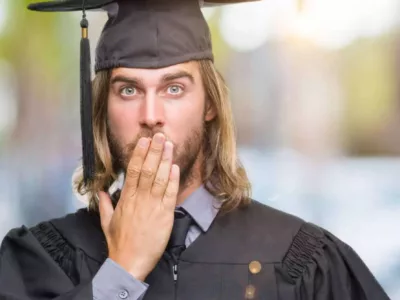 Ein Student in Doktorandentracht mit besorgtem Gesichtsausdruck, der seine Hand vor den Mund hält.