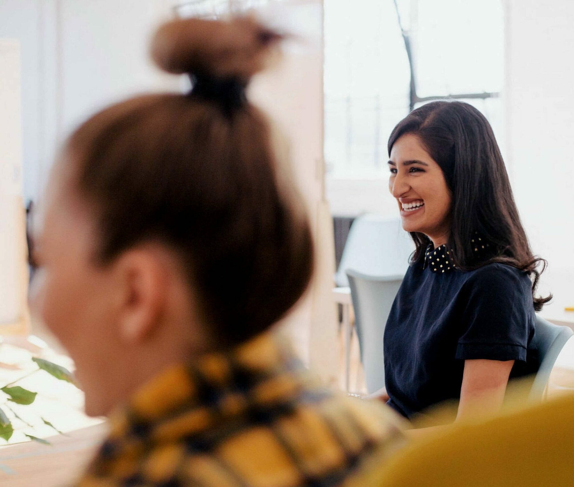 Eine Frau sitzt mit einem Lächeln im Gesicht an einem Tisch.