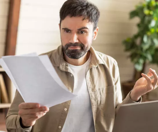 Das Bild zeigt einen Mann mit Bart, der offensichtlich frustriert ist, während er an einem Laptop in seinem Homeoffice arbeitet.