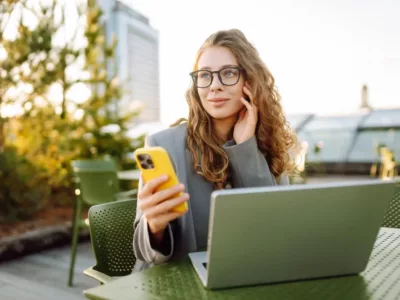 Studentin, die an einem Café sitzt. Sie trägt einen grauen Blazer und hat lockiges braunes Haar.