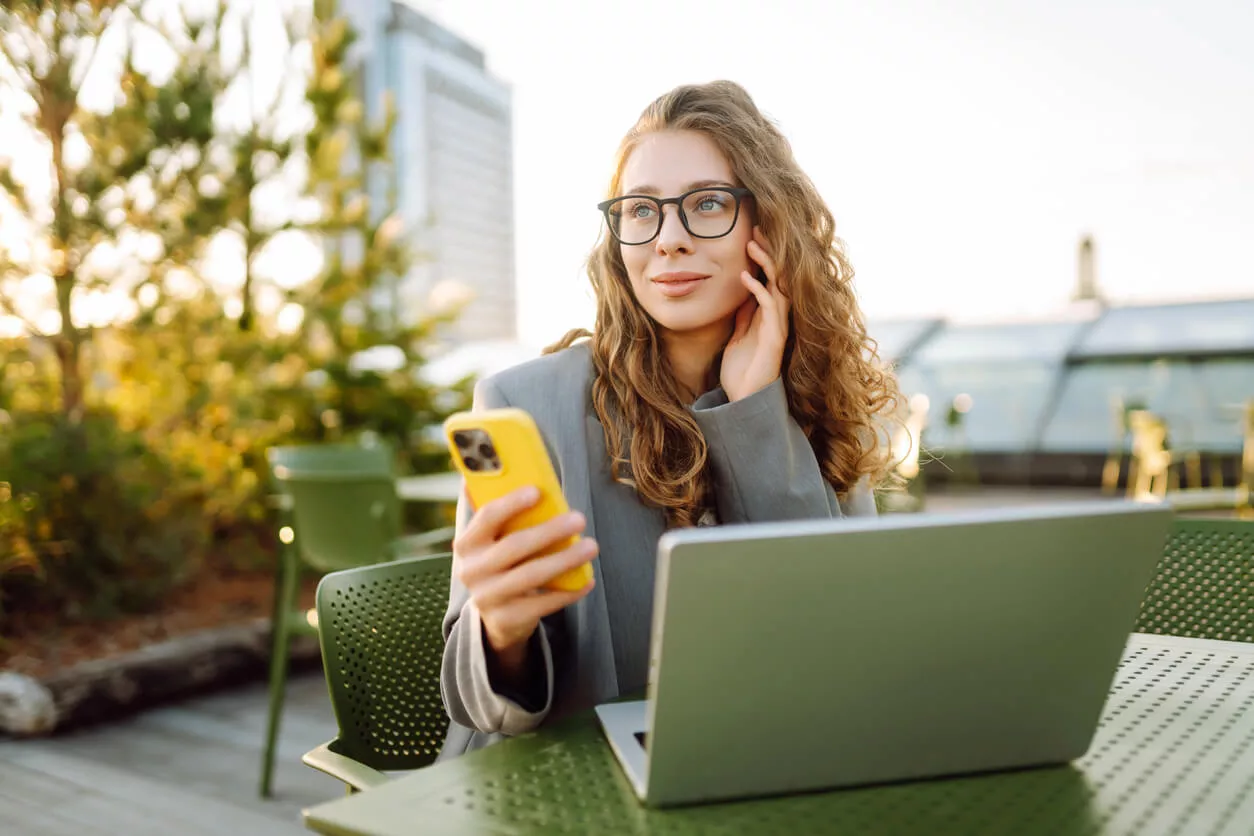 Studentin, die an einem Café sitzt. Sie trägt einen grauen Blazer und hat lockiges braunes Haar.