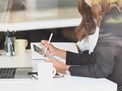 Eine Studentin, die an einem Schreibtisch sitzt und etwas auf einem digitalen Tablet schreibt.