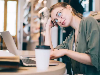 Studentin, die in einer Bibliothek oder einem Arbeitsbereich an einem Schreibtisch sitzt. Sie stützt ihren Kopf mit den Händen ab und sieht müde oder frustriert aus.