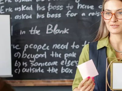 Lehrerin für Sprachen mit Post-it in der Hand vor Tafel im Unterricht