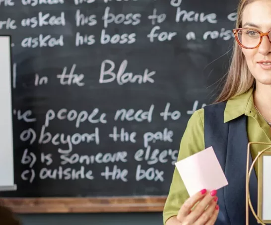 Lehrerin für Sprachen mit Post-it in der Hand vor Tafel im Unterricht