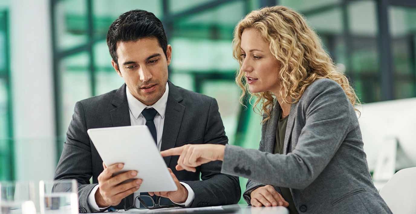 Zwei Geschäftsleute in einem modernen Büro betrachten gemeinsam ein Tablet und diskutieren Geschäftsangelegenheiten.