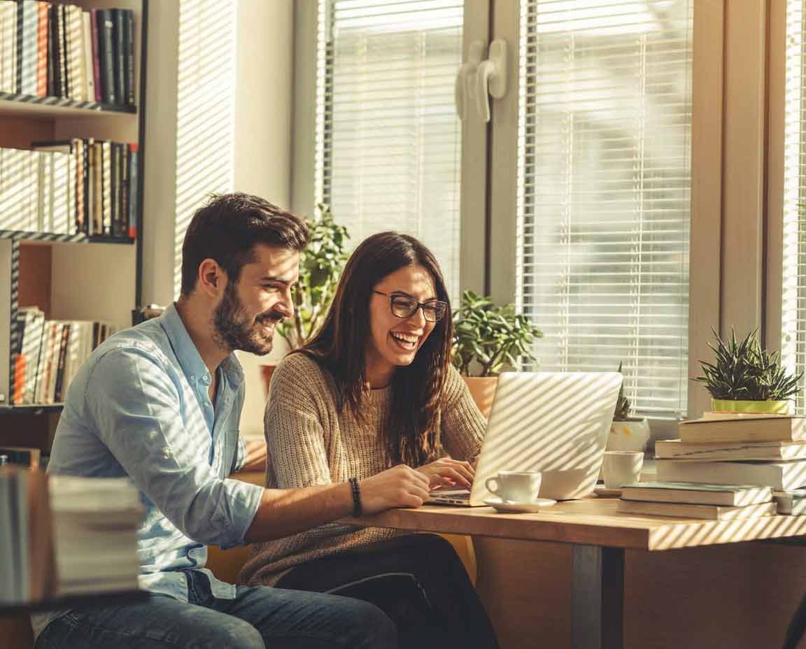 2 Studierende sitzen lachend zusammen vor einem Laptop