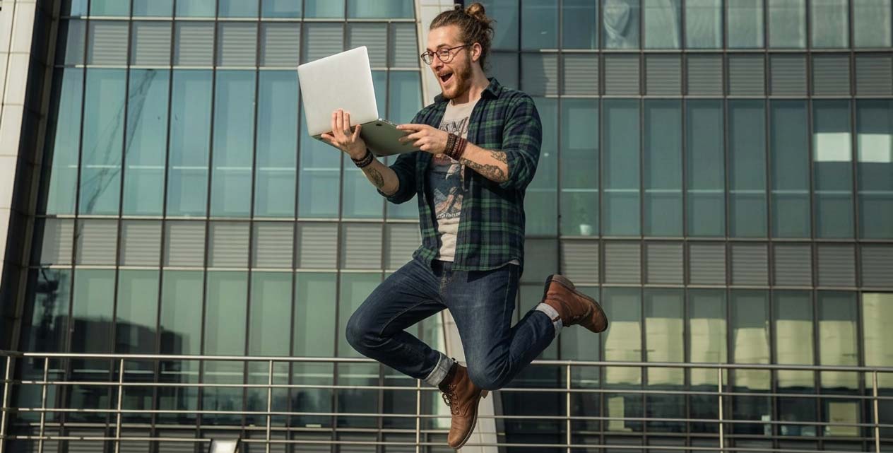 Student springt mit Laptop in der Hand in die Luft und freut sich