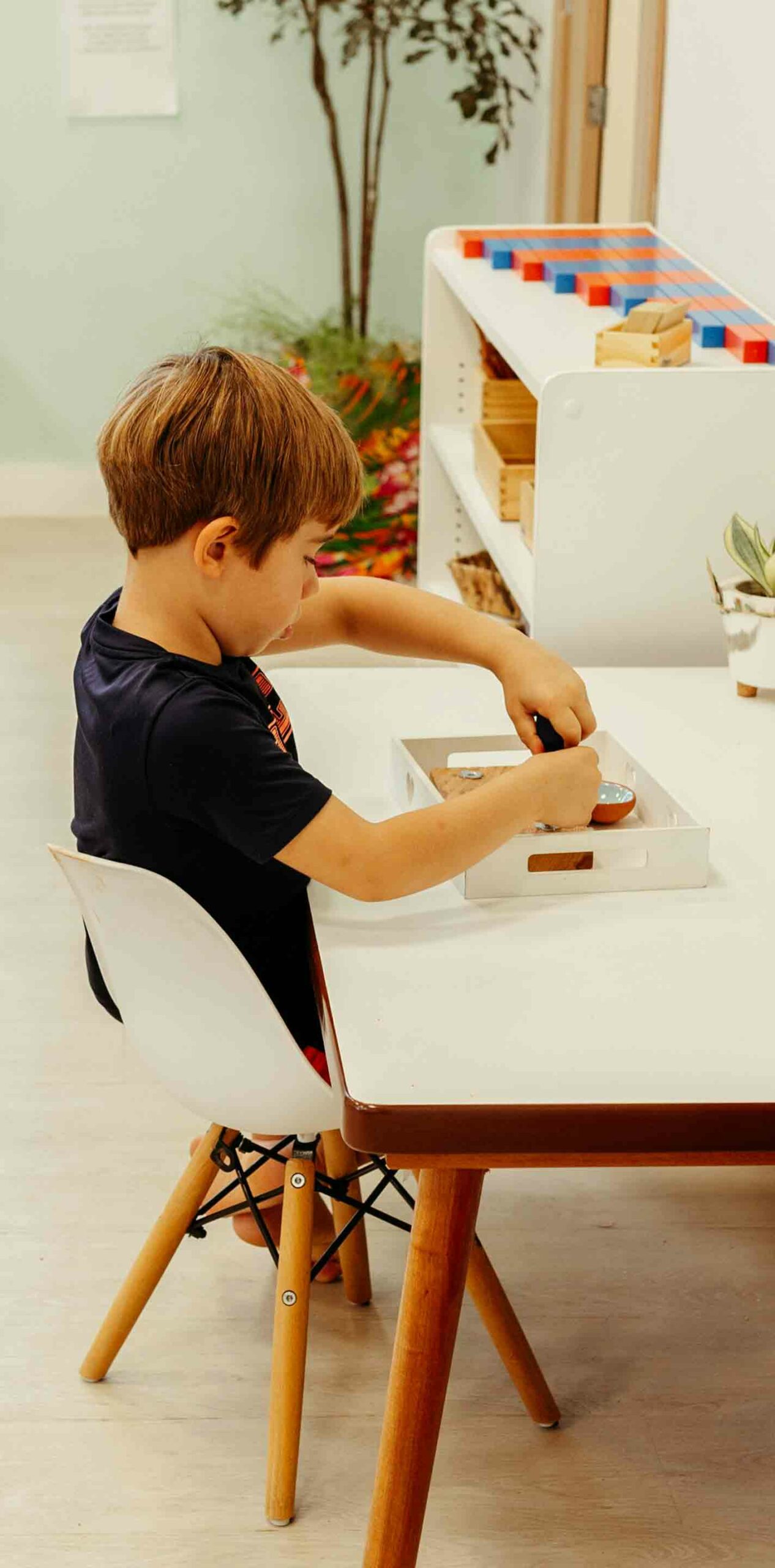 Kind arbeitet mit Montessori-Lernmaterialien an einem weißen Tisch in einer Klassenzimmerumgebung