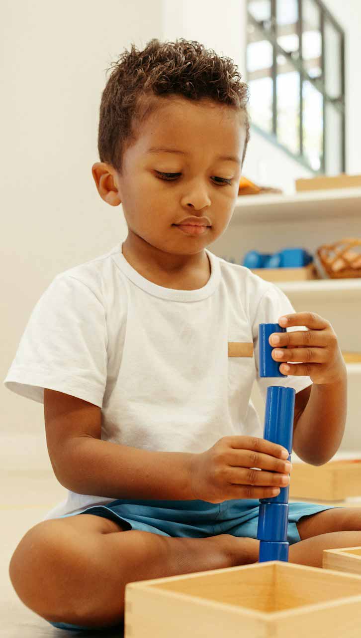 Kleiner Junge in weißem T-Shirt stapelt konzentriert blaue Bausteinen.