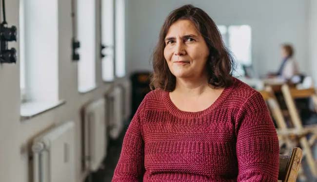 Prof. Dr. Verena Jung sitz mit einem blauen Buch auf einem Stuhl