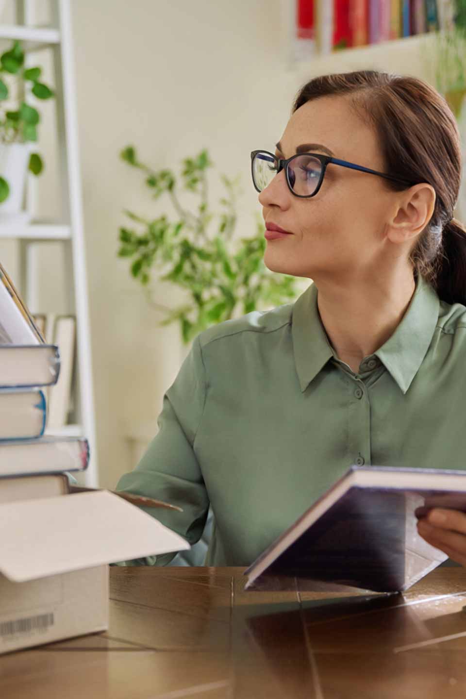 Eine Frau mit Brille und grünem Hemd sitzt am Schreibtisch mit Büchern.