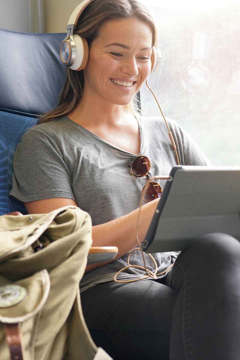 Eine lächelnde Frau mit Kopfhörern sitzt in einem Sessel und schaut auf ein Tablet.