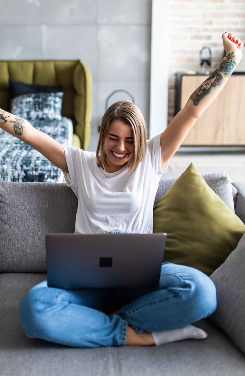 Studentin sitzt auf Sofa vor Laptop und jubelt.